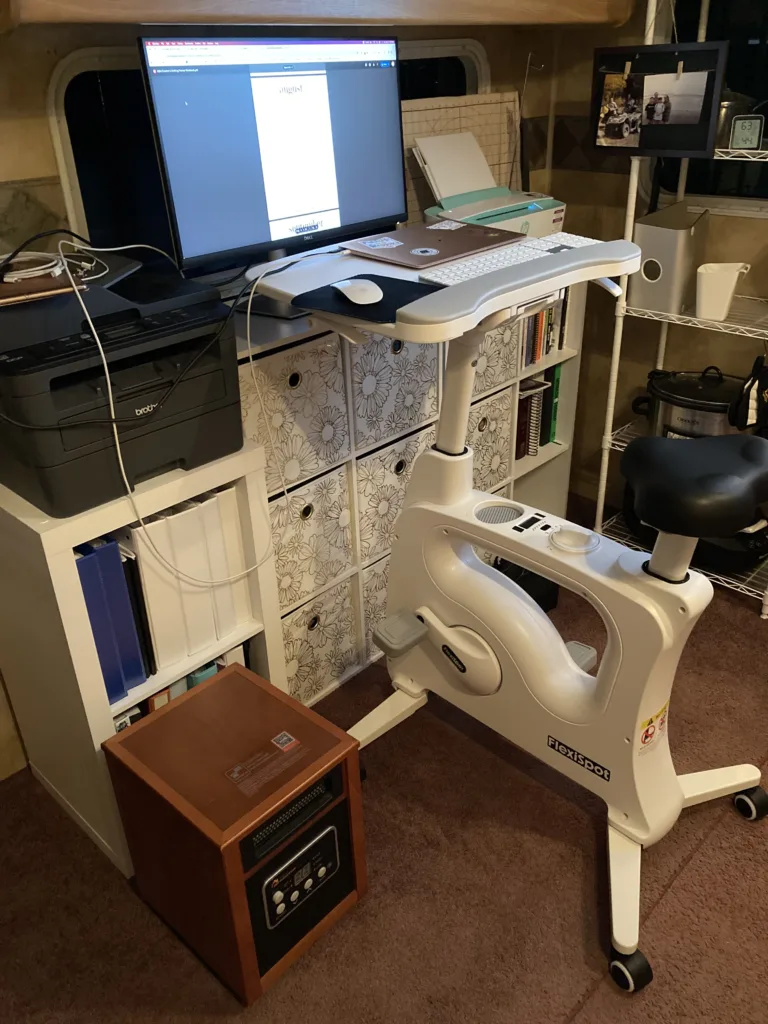 Bike desk with a laptop, keyboard, and mouse, in front of an external monitor with a printer on the left and a printer on the right. 